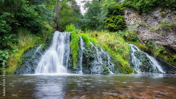 Fototapeta Crystal clear waterfall surrounded by greenery in the middle of the highlands of Scotland, UK.
