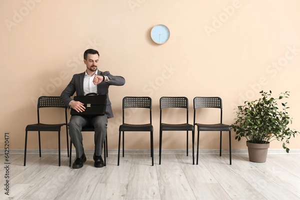 Fototapeta Young man looking at wristwatch while waiting for job interview in office
