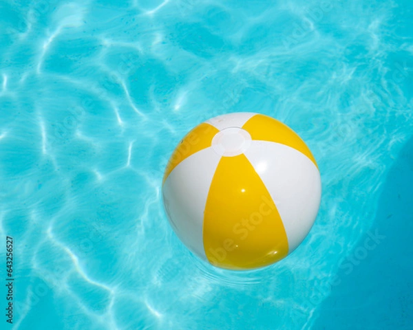 Obraz Beach ball, yellow and white, floating in cool blue pool water.