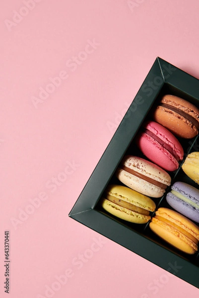 Fototapeta Dark green box with assorted macaroons on the pink background. Colorful desserts with different filling. Free space for text. Vertical photo.