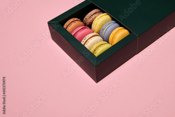 Fototapeta Dark green box with assorted macaroons on the pink background. Colorful desserts with different filling. Free space for text. Horizontal photo.