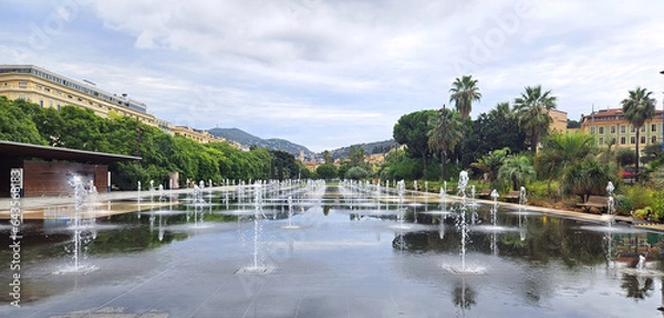 Fototapeta City fountain in the square, park in the city of Nice main square, Place Massena, during the day. Panoramic view of the mountainous part of the city, view on zoom. Cote d'Azur, France