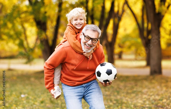 Fototapeta Portrait of happy grandfather and grandson with ball while playing football   in park.