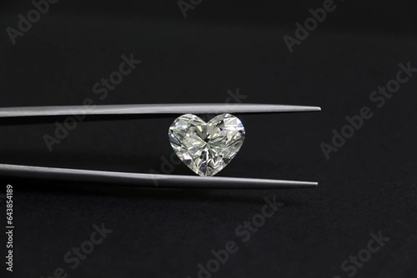 Obraz The big heart shape diamond in tweezers on black background