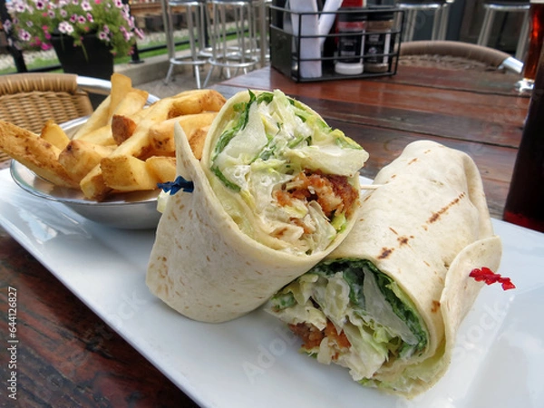 Obraz Chicken Caesar wrap, served with French fries, outside on the patio