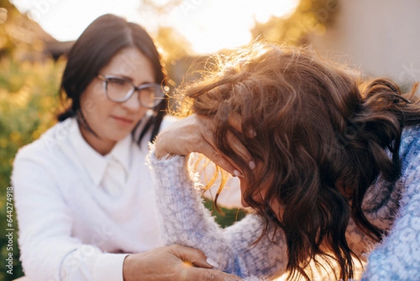 Obraz Concerned aged mother and adult daughter sitting on the sofa having a serious conversation, young woman talking to worried elderly mother, listening to her problems or concerns, helping cope with depr