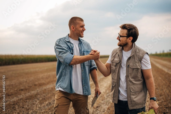 Fototapeta Front view of two men shaking hands in the field.