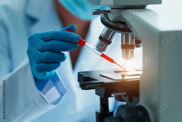 Obraz Close up dedicated hematology lab technician scrutinizing blood sample analysis under microscope, scientific laboratory research and drug testing concept, red color liquid