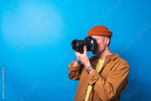 Fototapeta Happy smiling photographer taking pictures checking his camera settings in a studio shooting as content creator in blue background 