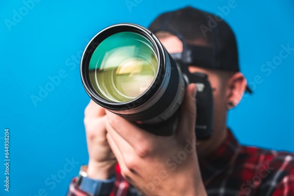 Fototapeta Happy photographer taking pictures covering his face with a camera with blank space for adds