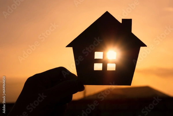 Obraz Hands holding paper house on sunset sky, family home, homeless housing, and home protection insurance concept, international day of families, new life, foster home care, and real estate.