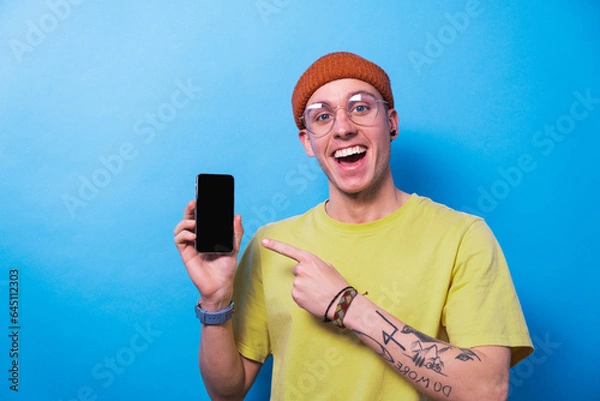 Fototapeta Happy young man smiling showing smartphone with empty screen, mockup for mobile app or website design