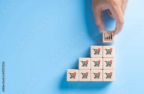 Fototapeta Hand holding wooden cube block stacking with investment increasing trend-up graph and shopping trolley cart. Increase higher sale volume for online e-commerce business marketing strategy concept.