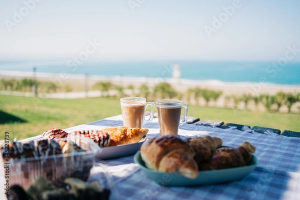 Fototapeta A picnic at the seaside beach. Breakfast with coffee, croissants and donuts by the ocean shore