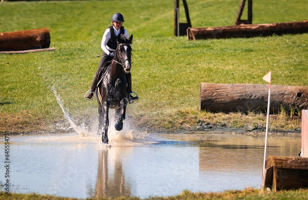 Fototapeta Horse with rider in an eventing tournament galloping through the water to the next jump..