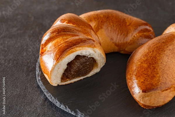 Fototapeta Tasty fresh crescent roll cut on slate stone plate round, dark background, selective focus