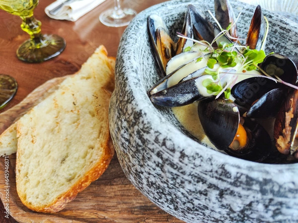 Obraz lunch at the restaurant. mussels stewed in cream sauce, garnished with herbs. served in a grey granite bowl with toasted bread