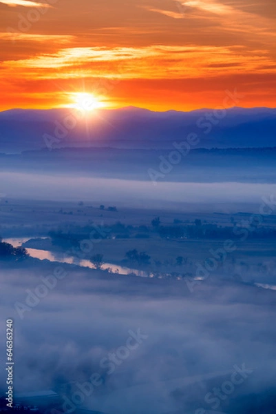 Fototapeta Aerial view of the sunrise over the valley in beautiful early morning mist in the highlands. Low clouds and fog cover the sleeping meadow. Hills valley mists landscape. Serene moment in rural area