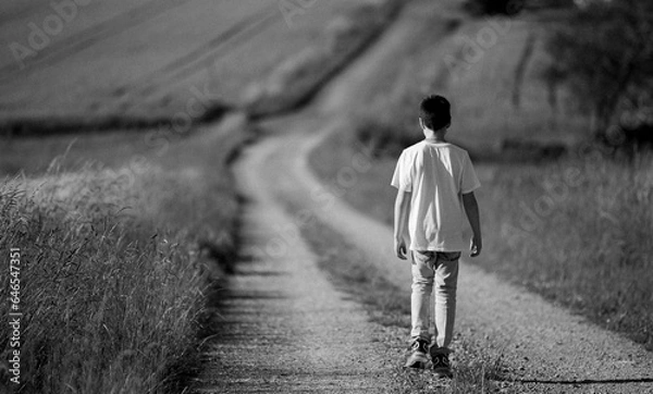 Obraz boy goes away. Teenage boy with backpack walking away on the rural road. 8 Year old boy walking away angry in to the woods. He was not happy about not going to the playground because of the time leak.