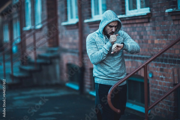 Fototapeta Young man looking at the time while getting ready to run in the city