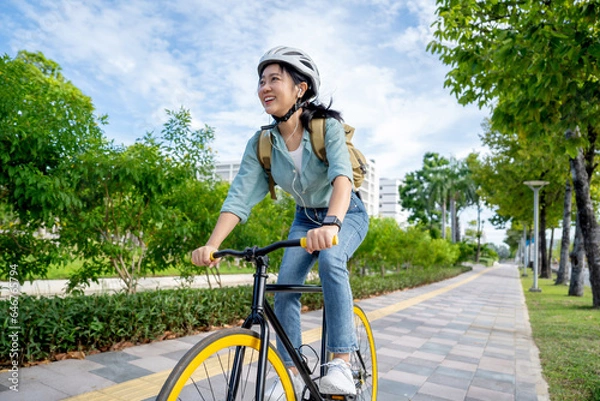 Fototapeta Happy young Asian woman while riding a bicycle in a city park. She smiled using the bicycle of transportation. Environmentally friendly concept.