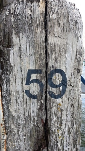 Obraz Brauner morscher und alter Holzpfahl im Hafen mit der Nummer 59 in schwarzer Schrift
