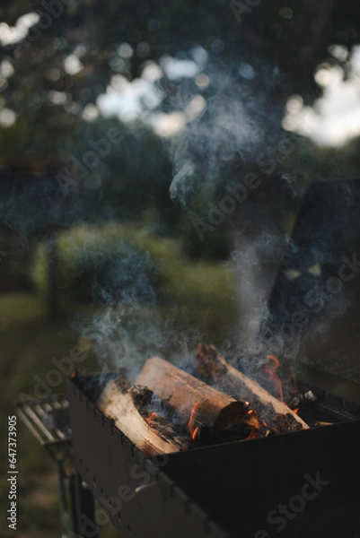 Fototapeta barbecue BBQ grill with flaming fire and ember charcoal on nature background, Flaming charcoal grill with open fire, ready for product placement. Concept of summer grilling, barbecue, bbq and party