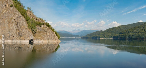 Fototapeta Panorama of lake with reflection of smooth lake surface and cloudy sky. Vidraru dam. Transfagarasan road. Romania