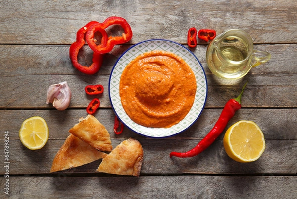 Fototapeta Plate of tasty muhammara and ingredients on wooden background