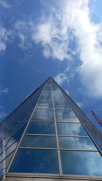 Obraz Glasfassade eines Wolkenkratzers vor blauem Himmel mit weißen Wolken