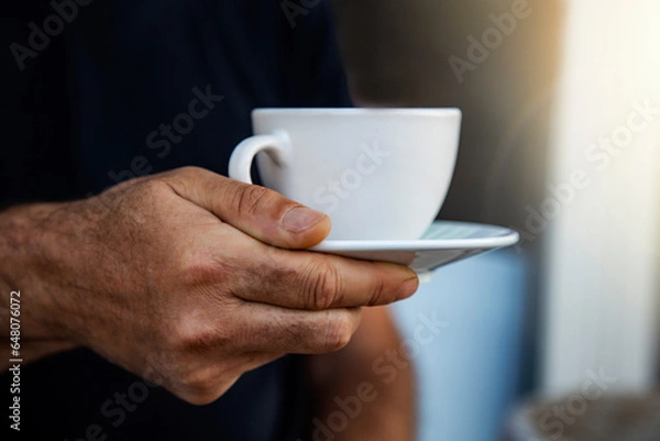 Obraz Close-up of man hand holding white cup of coffee or tea on black background. the mug with hot drink on a saucer