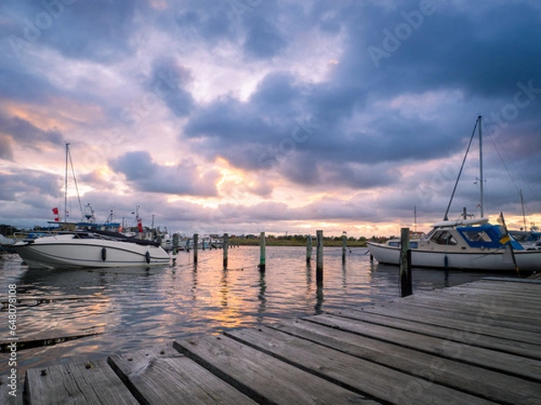 Fototapeta Wooden pier with boats in the evening light with thunderstorm approaching in the distance