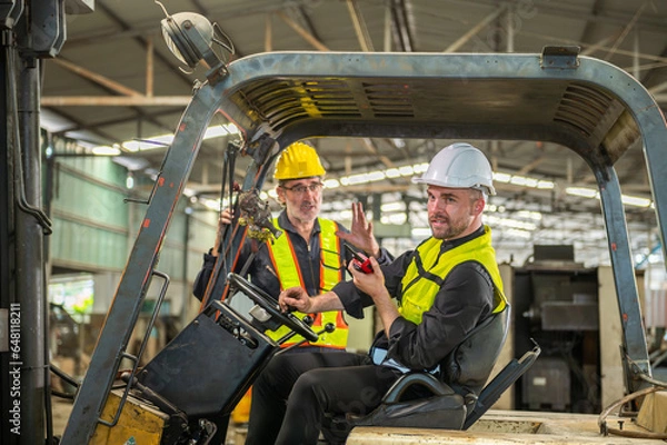 Fototapeta Portrait of forklift truck driver man smiling in old factory warehouse lifting pallet in storage shipping. forklift truck driver mail inside old forklift smiling to worker employee in warehouse store.