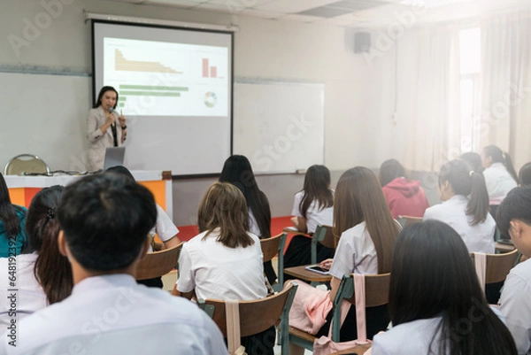 Fototapeta Rear view of college students listen to teacher teaching and explaining lesson in classroom