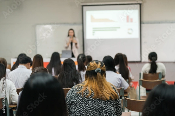 Fototapeta Rear view of college students listen to teacher teaching and explaining lesson in classroom
