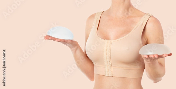 Obraz Woman wearing compressing bra after breast augmentation. Holding round implants