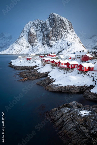 Fototapeta Vertical photo of Hamnoy fishing village in Norway. Lofoten winter scene with typical red houses and a snowy mountain in the background.