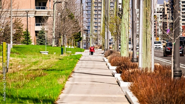 Fototapeta A woman in a red coat is walking on the sidewalk by the roadside.