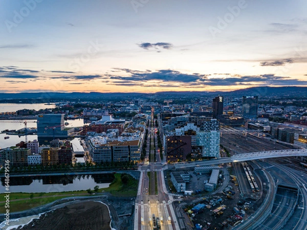 Obraz Aerial view of modern urban borough at Central train station against colourful sunset sky. Calm water surface reflecting sky. Oslo, Norway