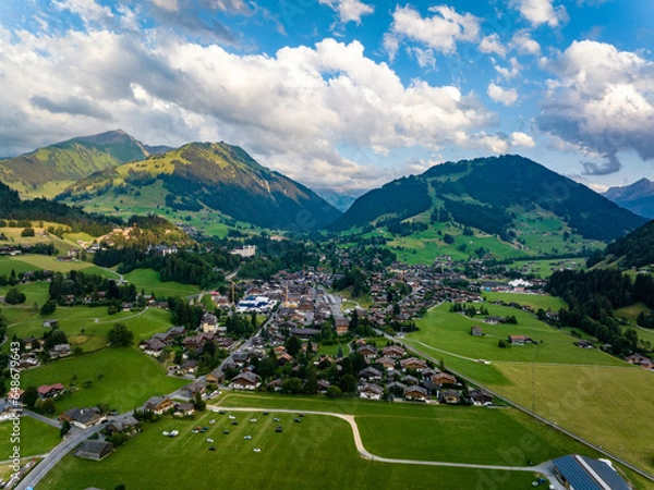 Obraz Aerial shot of beautiful alpine landscape with town, hills and deep valleys. Picturesque golden hour in mountains. Gstaad, Switzerland