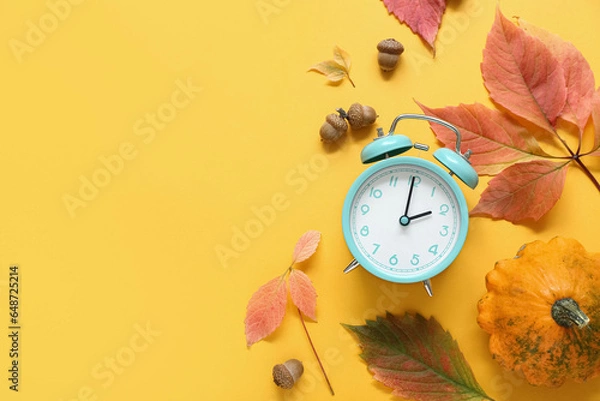 Fototapeta Alarm clock with autumn leaves and pumpkin on orange background
