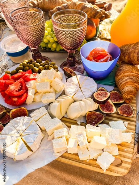 Obraz festive party setting with variety of cheeses, olives, poidos, grapes, croissants, figs and glasses of wine on the beach. valentine's day picnic with cheeses and fruits on the beach