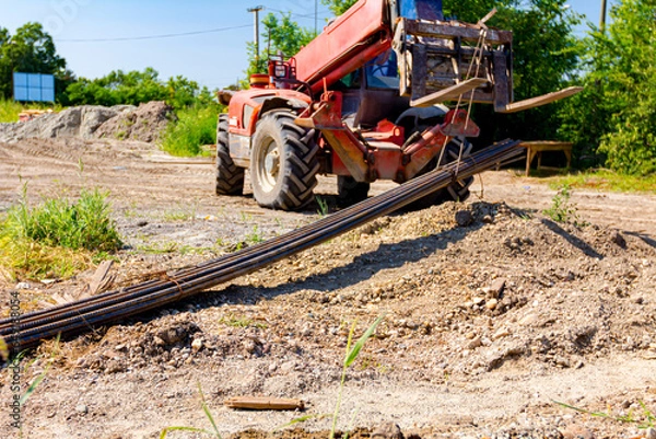 Fototapeta Forklift lifts the rebar bundle from ground on building site