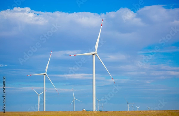 Fototapeta Fleet of power generators in motion. The blades of the wind farm rotate against the sky. The concept of extracting electricity from renewable sources. Wind turbine to generate electricity.