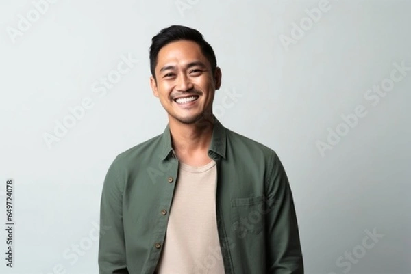 Fototapeta medium shot portrait of a happy Filipino man in his 30s wearing a chic cardigan against a minimalist or empty room background