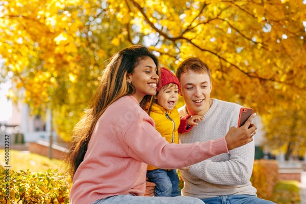 Fototapeta A happy family with a smiling child takes a selfie with autumn leaves
