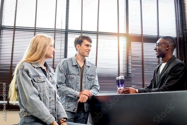 Fototapeta Cute couple lover sitting by table in bar having cocktail drink and friendly African bartender standing behind counter bar making drinks to serve customers, happy people enjoying at night club lounge.