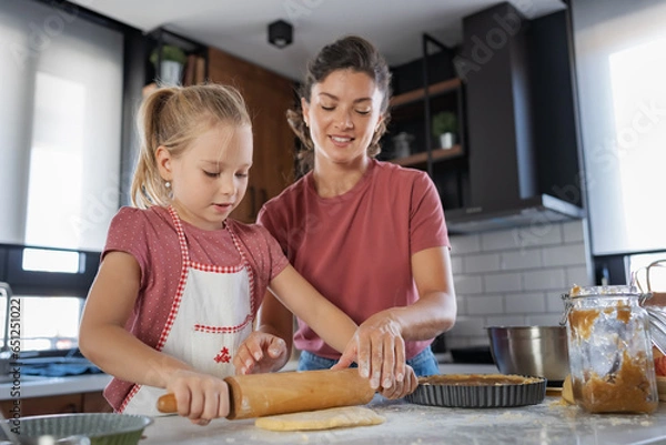 Fototapeta Beautiful happy mother and daughter preparing an apple pie at home kitchen. Autumn fun family activities