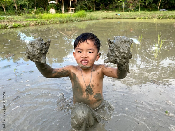 Obraz Thailand Asia boy is enjoy playing in the mud of rice field. Outdoor kid learning activity.