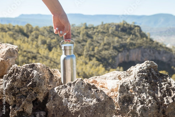 Obraz Hand taking an aluminum thermal bottle to hydrate on a hiking trail